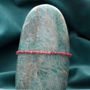 Bransoletka damska pozłacana z kamieniem naturalnym różowy turmalin na sznurku w szarym kolorze zawieszona na kamieniu