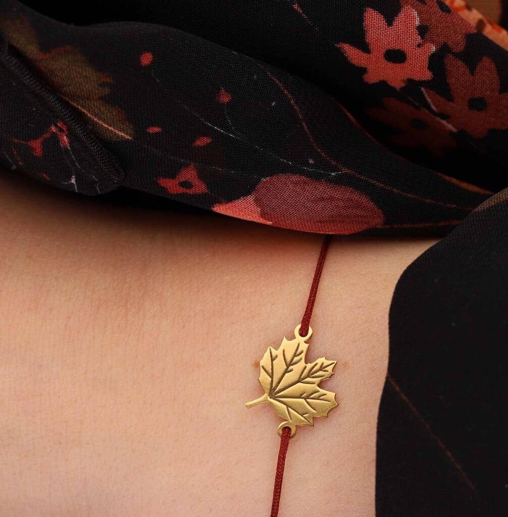 Bransoletka na jesień z liściem klonu srebrna pozłacana na bordowym sznurku założona na ręce