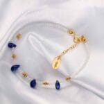 Damska bransoletka z kamieniami naturalnymi kianit kamień księżycowy wykonana ze srebra 925 pozłacanego leżąca na płótnie. Bransoletka regulowana za pomocą przedłużki na łańcuszku