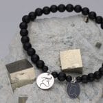 Elastyczna męska bransoletka z kulek czarnego agatu oraz srebra próby 925 z celebrytkami z grawerem głowy niedźwiedzia i byka, leżąca na pirycie