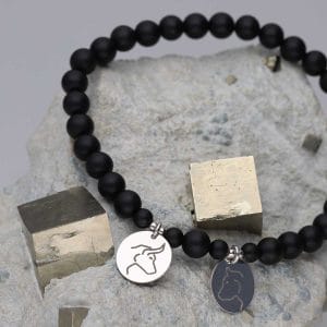 Elastyczna męska bransoletka z kulek czarnego agatu oraz srebra próby 925 z celebrytkami z grawerem głowy niedźwiedzia i byka, leżąca na pirycie