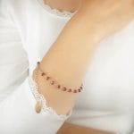 bransoletka damska srebrna pozłacana łancuszkowa z rubinem założona na rękę. Bransoletka posiada przedłużkę na której końcu zawieszona jest zawieszka z logo Rosett