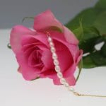 Elegancka delikatna bransoletka damska srebrna pozłacana na łańcuszku z perłami naturalnymi położona na rózy