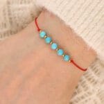 Bransoletka na czerwonym sznureczku z niebieskim kamieniem turkus na ręce
