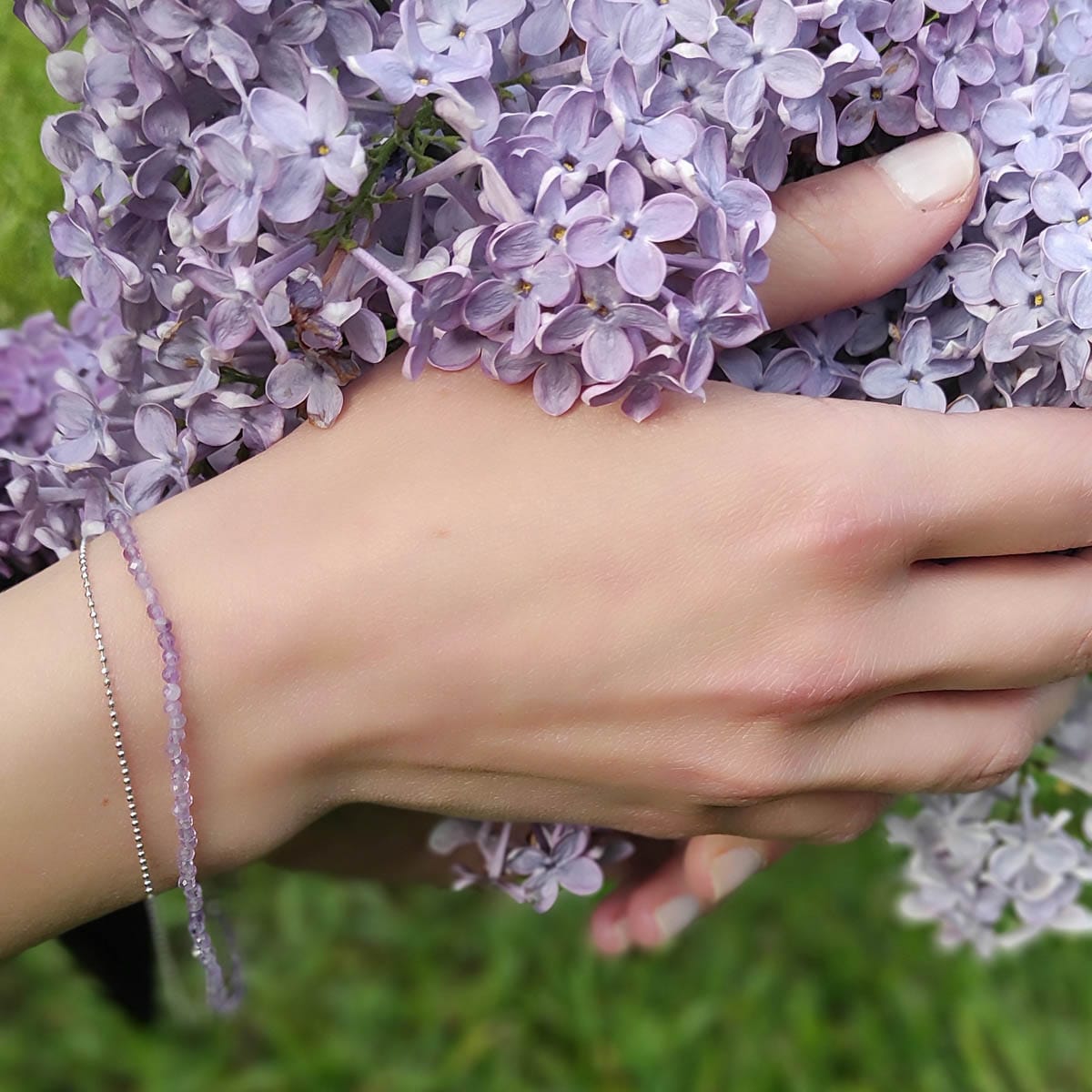 Bransoletka srebrna dla kobiety z kuleczkami ametystu oraz dodatkowym łańcuszkiem ze srebra. Bransoletka założona na ręce