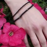 Zestaw bransoletek damskich srebrnych pozłacanych z czarnym onyksem. Bransoletki założone na ręce wśród kwiatów