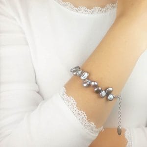 Stylowa bransoletka damska srebrna z perłami ubrana na ręce. Bransoletka posiada przedłużkę na której końcu zawieszona jest zawieszka z logo Rosett