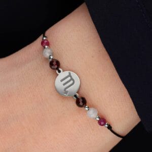 Srebrna bransoletka dla Skorpiona na czarnym sznurku z celebrytką, granatem, akwamarynem i rubinem założona na ręce