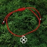 Damska bransoletka na szczęście leżąca na mchu. Bransoletka z czerwonego sznurka i celebrytki w kształcie czterolistnej koniczynki. Celebrytka ze srebra 925