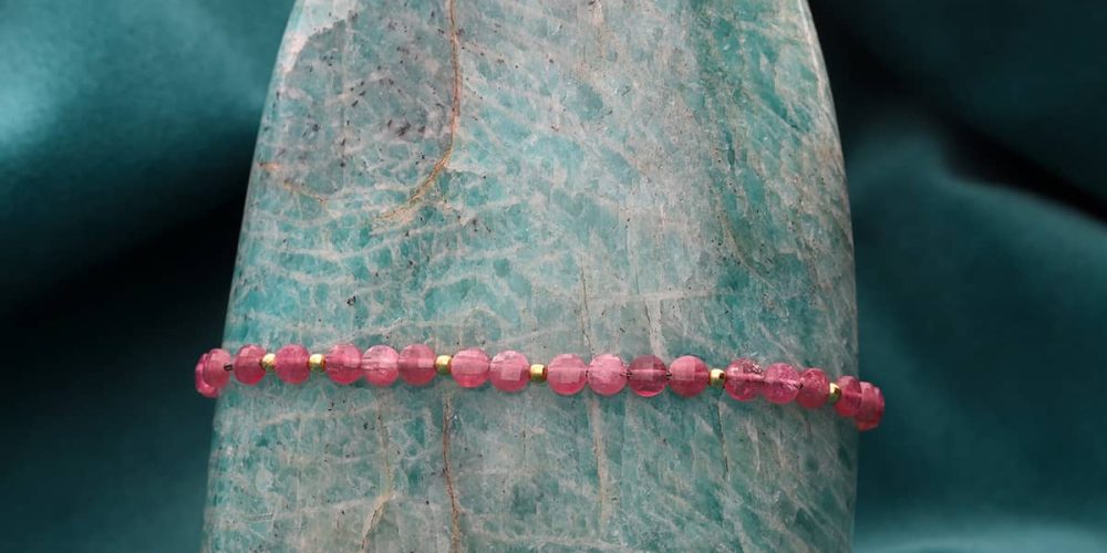 Bransoletka damska pozłacana z kamieniem naturalnym różowy turmalin na sznurku w szarym kolorze zawieszona na kamieniu