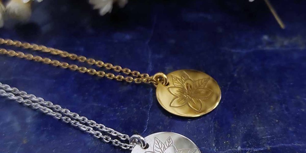 Dwa naszyjniki celebrytka z kwiatami w formie srebrnej i pozłacanej. Naszyjniki leżą na lapis lazuli