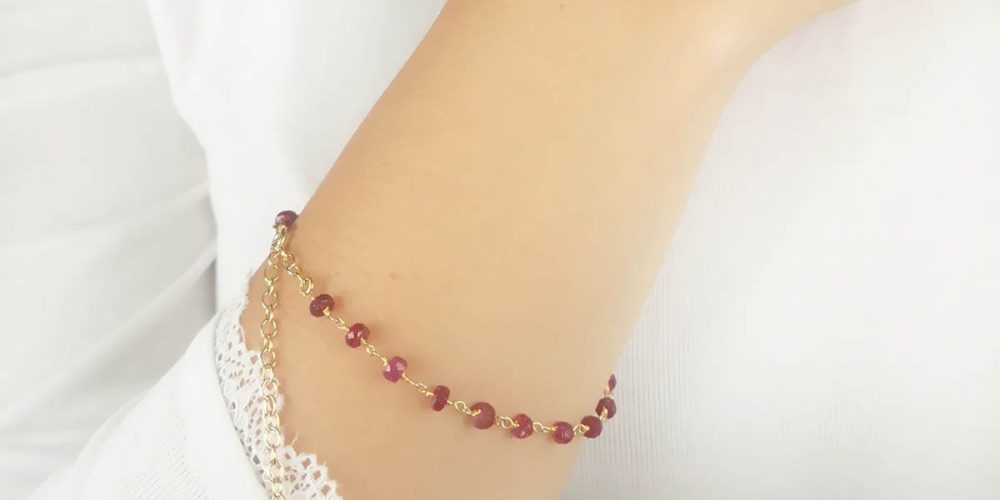 bransoletka damska srebrna pozłacana łancuszkowa z rubinem założona na rękę. Bransoletka posiada przedłużkę na której końcu zawieszona jest zawieszka z logo Rosett