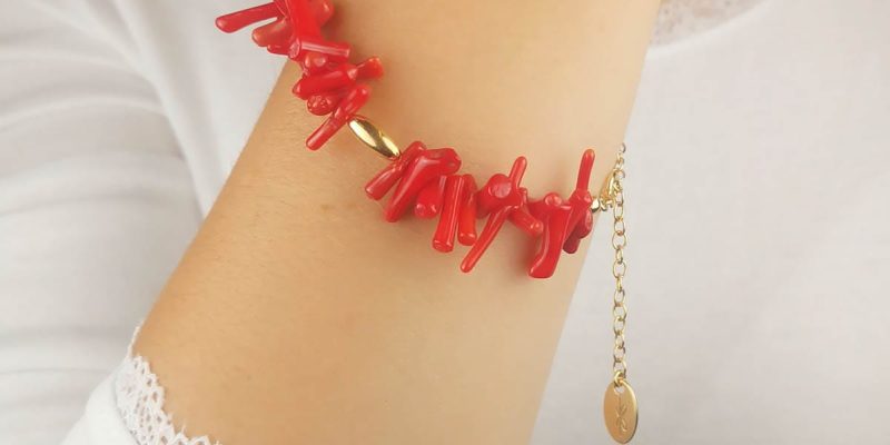 Damska bransoletka srebrna pozłacana z słupkami korala czerwonego założona na rękę. Bransoletka posiada przedłużkę na której końcu zawieszona jest zawieszka z logo Rosett