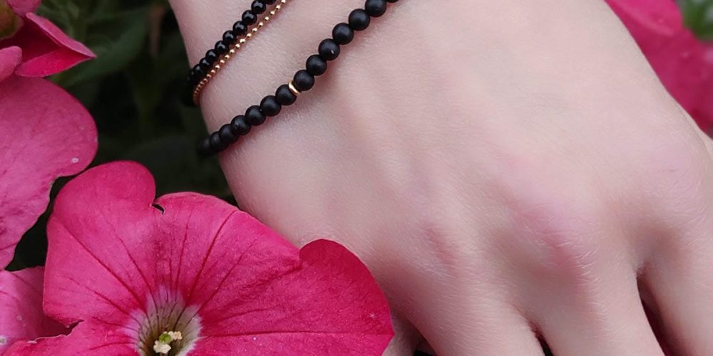 Zestaw bransoletek damskich srebrnych pozłacanych z czarnym onyksem. Bransoletki założone na ręce wśród kwiatów