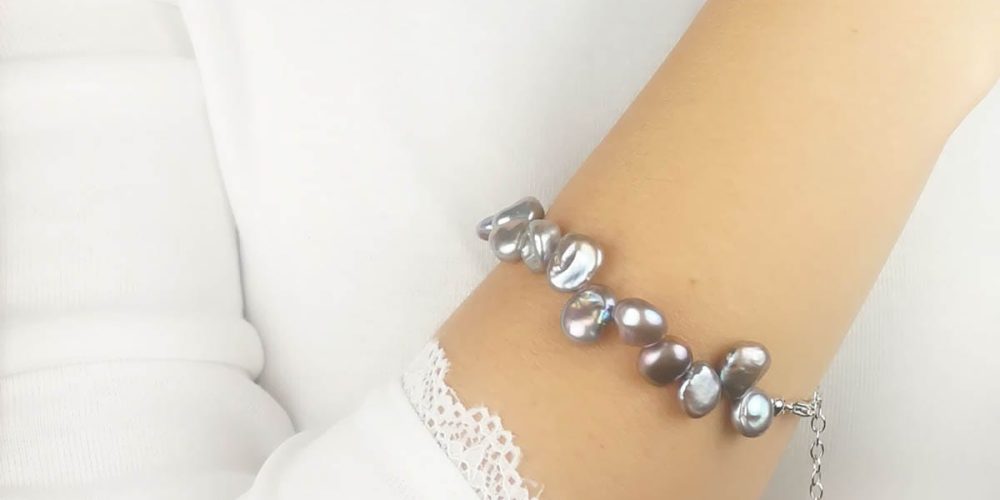 Stylowa bransoletka damska srebrna z perłami ubrana na ręce. Bransoletka posiada przedłużkę na której końcu zawieszona jest zawieszka z logo Rosett