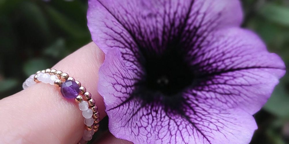 pierścionek elastyczny gold filled z ametystem, kamieniem księżycowym na palcu wśród kwiatów