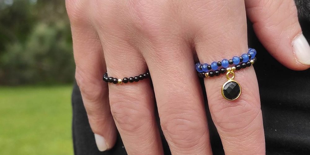 Złoty pierścionek elastyczny z kuleczką złota i czarnym onyksem i innymi pierścionkami elastycznymi założone na palcu