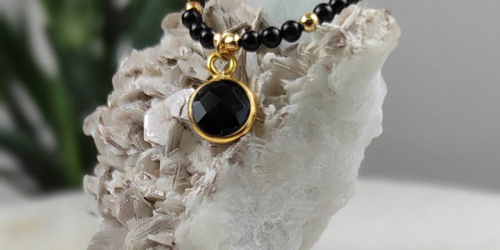 pierścionek srebrny pozłacany elastyczny z kuleczek onyksu i zawieszką z onyksem w okuciu srebrnym zawieszony na skale z kryształem akwamarynu