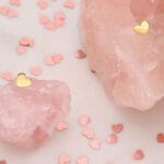 surowe bryłki kwarcu różowego - kamienia na miłóść na których położone są kolczyki sztyfty serca