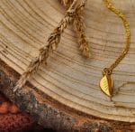 Damski naszyjnik srebrny pozłacany z motywem liścia leżący na tacy z drewna
