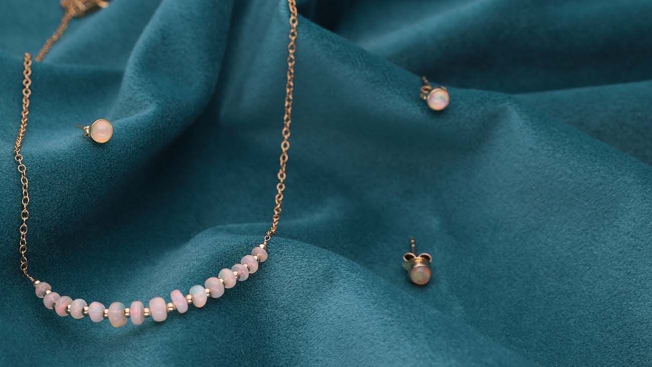 biżuteria z opalem: damski naszyjnik srebrny pozłacany i kolczyki sztyfty z opalem leżące na zielonym płótnie