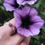 pierścionek elastyczny gold filled z ametystem, kamieniem księżycowym na palcu wśród kwiatów