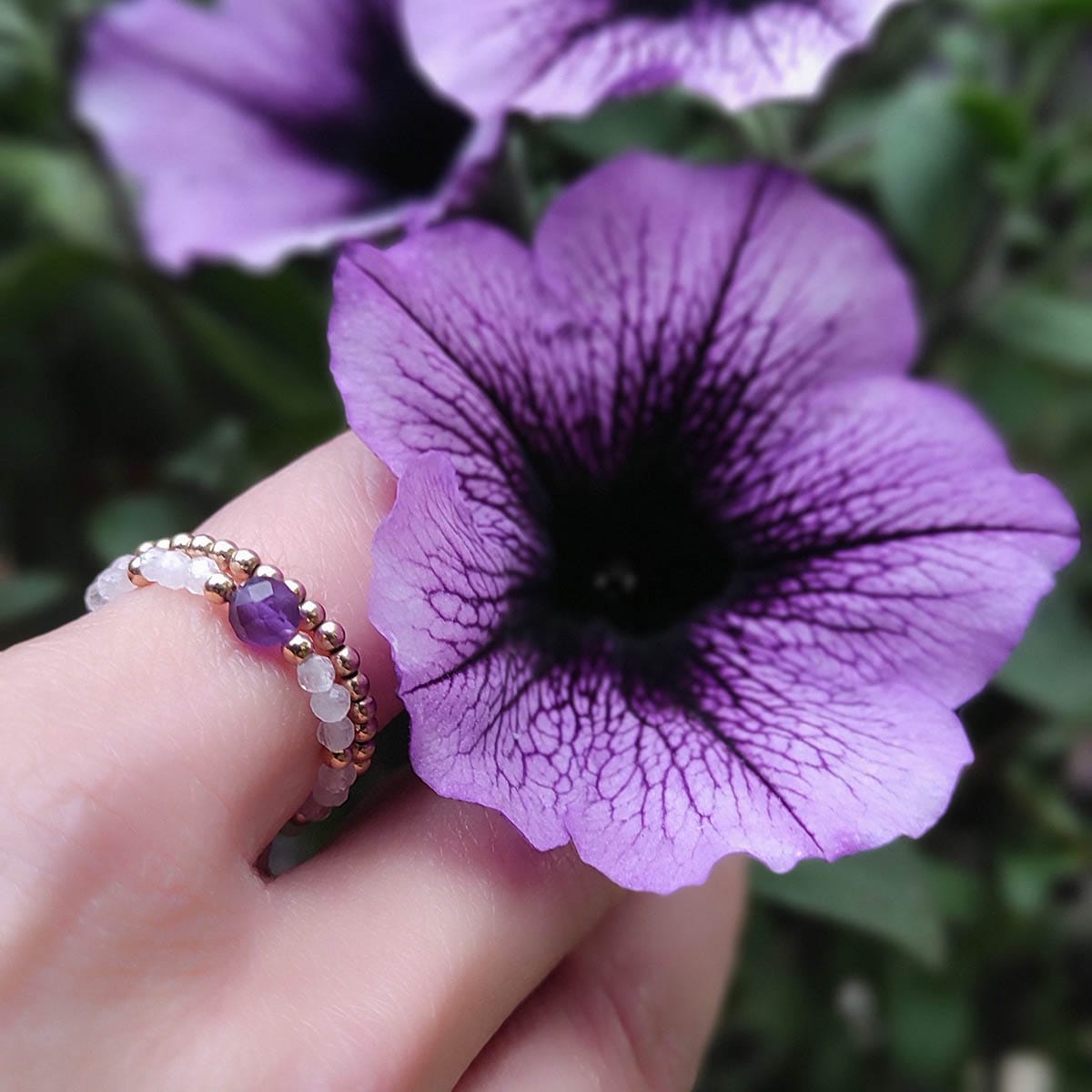 pierścionek elastyczny gold filled z ametystem, kamieniem księżycowym na palcu wśród kwiatów