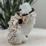 pierścionek srebrny pozłacany elastyczny z kuleczek onyksu i zawieszką z onyksem w okuciu srebrnym zawieszony na skale z kryształem akwamarynu